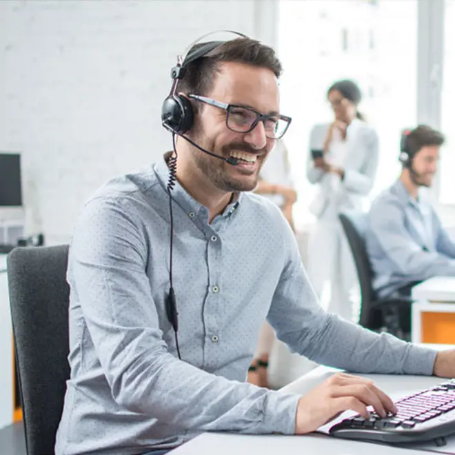 image of a smiling man at desk with headphones on customer support